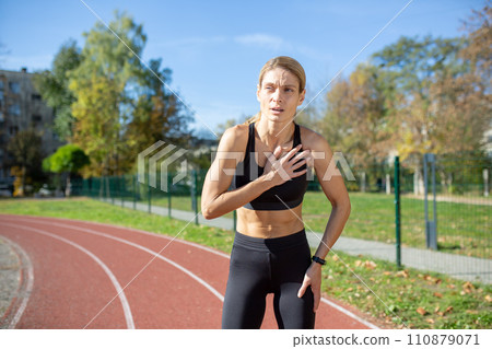 Focused sportswoman taking a break on running track, hands on knees, feeling exhaustion after sprint. Concept of determination and fitness training. 110879071
