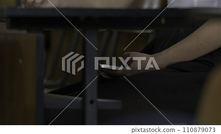 Woman hand using a smart phone under a wooden table. Woman uses the Internet on your phone during the exam 110879073