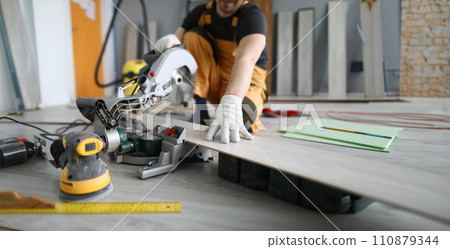 Repairman sawing laminate panels floor in room 110879344
