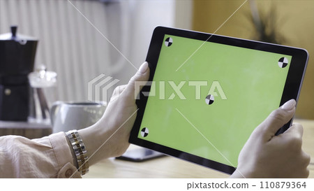 Young woman sitting at the table and looking at the computer tablet with the chroma key green screen. Stock footage. Chroma key screen for placement of your own content. 110879364