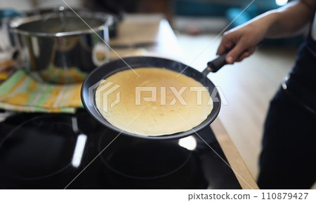 Hand holds pan with pancake, cooking at home 110879427