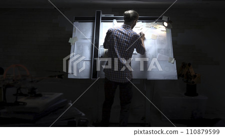 Man in writing drawing something on chalkboard,back view. Back view man looking at white wall with hand-drawn sketches related to economics and statistics 110879599