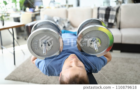 Strong man doing exercises with dumbbells on carpet Strong man doing exercises with dumbbells on carpet 110879618
