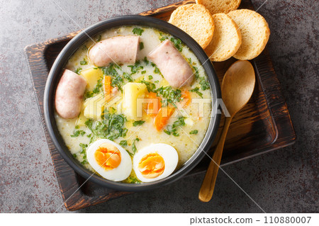 Zurek Traditional Polish soup on rye sourdough with sausage and egg close-up in a bowl. Horizontal top view Zurek Traditional Polish soup on rye sourdough with sausage and egg close-up in a bowl. Horizontal top view 110880007