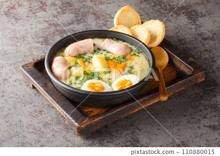 Polish Sour Rye Soup Zurek with white sausage, boiled egg and fresh veggies close-up in a bowl. Horizontal Polish Sour Rye Soup Zurek with white sausage, boiled egg and fresh veggies close-up in a bowl. Horizontal 110880015