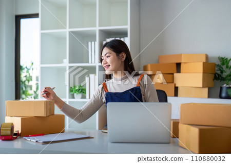 Young woman working online ecommerce shopping at her shop. Young woman sell prepare parcel box of product for deliver to customer. Online selling, ecommerce. Selling products online 110880032
