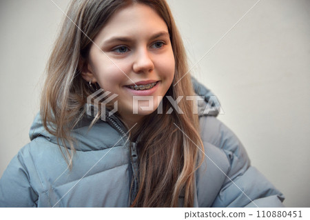 Close-up portrait of cute smiling teenage girl with braces wearing in warm coat looking away against blurred background. Selective focus. 110880451