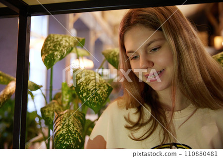 Portrait of cute girl smiling with teeth in dental braces while looking in smartphone against blurred background. Cozy indoor setting. Portrait of cute girl smiling with teeth in dental braces while looking in smartphone against blurred background. Cozy indoor setting. 110880481