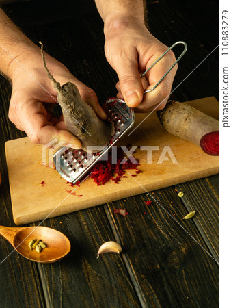 Close-up of a cook hands grating red beets to prepare a vegetarian dish. Concept of cooking vegetables on kitchen table in restaurant 110883279