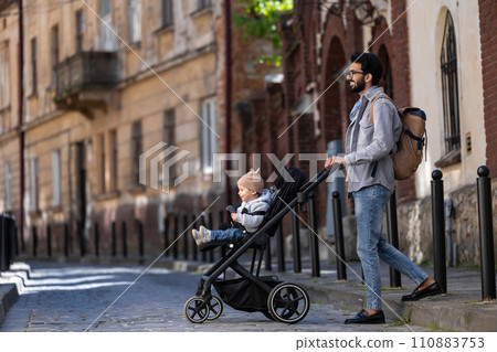 Dark-haired tall man with a baby carriage in the city street Dark-haired tall man with a baby carriage in the city street 110883753