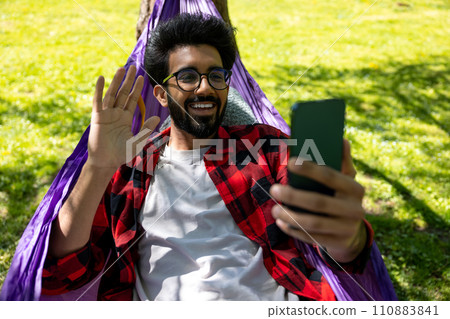 Contented hindu young man talking on the phone and laying in hammock Contented hindu young man talking on the phone and laying in hammock 110883841