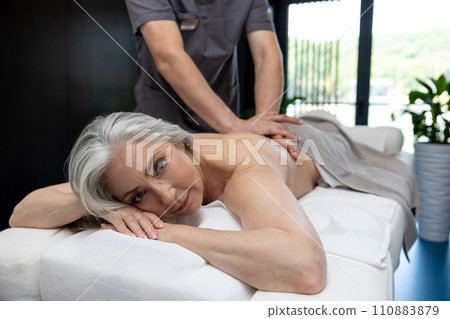 Gray-haired mature woman lying on a couch and having session of back massage 110883879