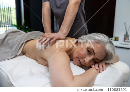 Gray-haired mature woman lying on a couch and having session of back massage Gray-haired mature woman lying on a couch and having session of back massage 110883891