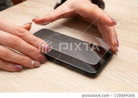 Woman's hand putting protective glass on smartphone 110884168