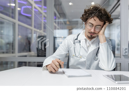 A doctor in a white coat sits at a table with a stethoscope in his hand. A doctor in a white coat sits at a table with a stethoscope in his hand. 110884201