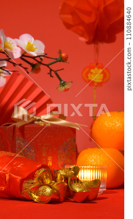 Chinese Lunar New Year background, red theme. gold in silk bag, red gift box with golden bow, paper fan, oranges, plum blossom branch, candle and red floating lantern sway for celebrate. vertical Chinese Lunar New Year background, red theme. gold in silk bag, red gift box with golden bow, paper fan, oranges, plum blossom branch, candle and red floating lantern sway for celebrate. vertical 110884640