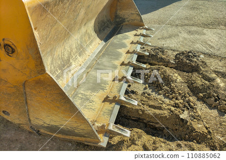 An empty excavator bucket with numerous scratches and paint chips, over a buried trench. Concept of construction, repair work related to digging the ground, excavation of soil An empty excavator bucket with numerous scratches and paint chips, over a buried trench. Concept of construction, repair work related to digging the ground, excavation of soil 110885062