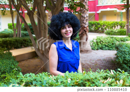 Portrait of a woman with black curly hair and a beautiful smile in a blue dress Portrait of a woman with black curly hair and a beautiful smile in a blue dress 110885410