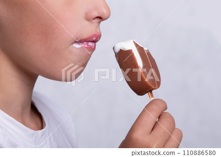 A boy whose face is unrecognizable eats ice cream covered in chocolate. 110886580