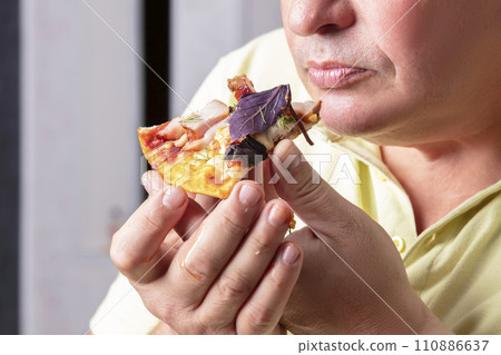 The man's hands hold a piece of pizza to his mouth. The man's hands hold a piece of pizza to his mouth. 110886637