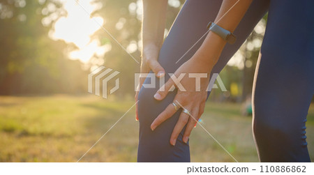 woman with knee pain in evening park. hold her sports injured knee. Low section of sports female suffering from joint pain while standing on track during. Accident from exercise concept. woman with knee pain in evening park. hold her sports injured knee. Low section of sports female suffering from joint pain while standing on track during. Accident from exercise concept. 110886862
