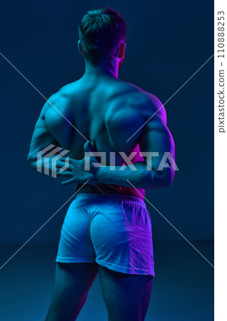 Muscular male back. model clasped hands behind back in neon light. Mab wearing denim jeans. Gel portraits. Muscular male back. model clasped hands behind back in neon light. Mab wearing denim jeans. Gel portraits. 110888253