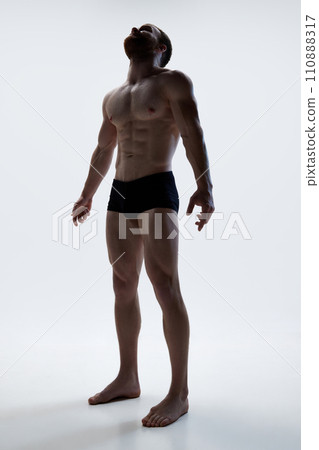Young athlete man in underwear posing against white background. Male athlete model with naked torso and packs of abs. Young athlete man in underwear posing against white background. Male athlete model with naked torso and packs of abs. 110888317