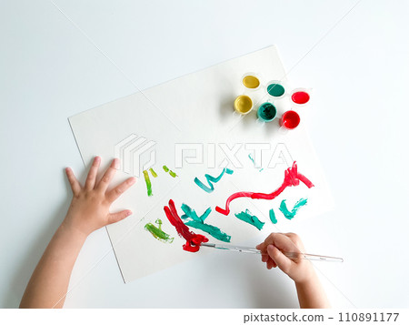 small child draws with paints and brush on white table. 110891177