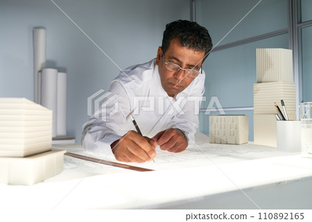 Portrait of mature Indian architect drawing blueprints at workstation in office, copy space Portrait of mature Indian architect drawing blueprints at workstation in office, copy space 110892165
