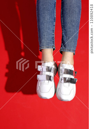 Woman's legs in jeans and white sneakers on red background Woman's legs in jeans and white sneakers on red background 110892418