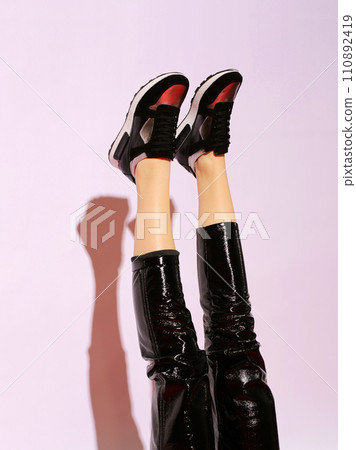 Female legs in black leather pants and black sneakers on pink background with hard light upside down. Female legs in black leather pants and black sneakers on pink background with hard light upside down. 110892419
