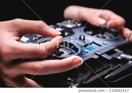 Remote control of FPV racing drone on black background in female hands, close-up Remote control of FPV racing drone on black background in female hands, close-up 110892917