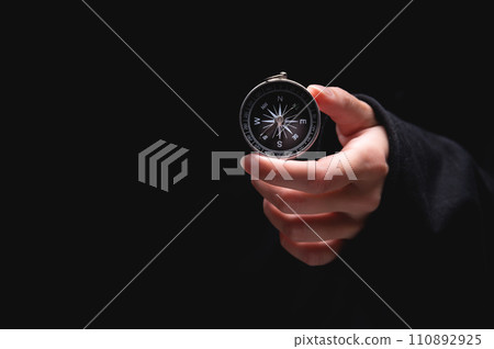 woman hand holds a compass showing south on a black background. A hand from the darkness holds out a compass, the concept of being lost and finding a solution or ideas with meanings woman hand holds a compass showing south on a black background. A hand from the darkness holds out a compass, the concept of being lost and finding a solution or ideas with meanings 110892925