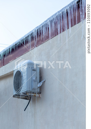The conditioner covered with icicles on a yellow wall. The conditioner covered with icicles on a yellow wall. 110893092