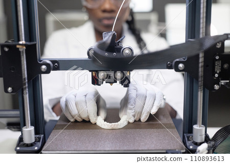 Close up shot of female technicians gloved hands adjusting teeth prosthesis on 3D printer hot bed in engineering laboratory 110893613