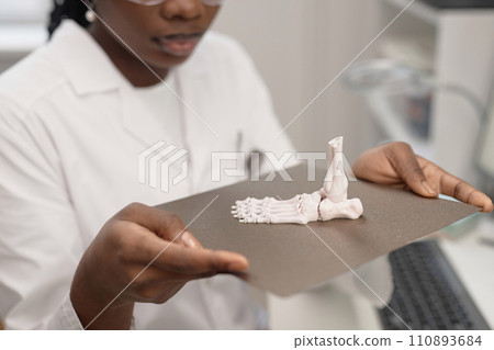 Close up shot of produced white human foot bone prototype on top of 3D printer metal hot bed in hands of Black woman laboratory technician 110893684