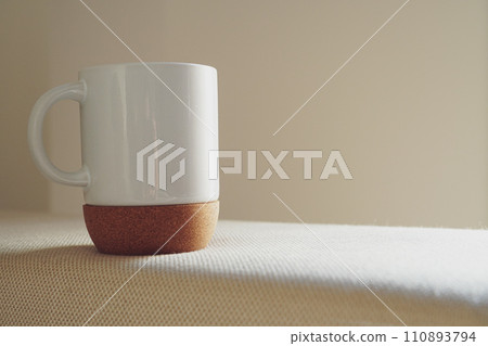A white mug with a cork bottom on a white sofa 110893794