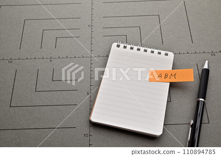 A sticky note with the abbreviation ABM written on it is pasted on a notepad. A sticky note with the abbreviation ABM written on it is pasted on a notepad. 110894785