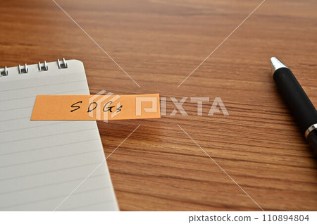 A sticky note with SDGs written on it is pasted on a memo pad. 110894804