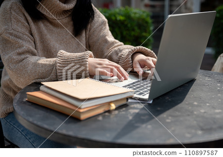 Cropped shot of an Asian woman working remotely outdoors, working on her laptop computer. Cropped shot of an Asian woman working remotely outdoors, working on her laptop computer. 110897587