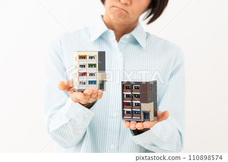 A middle-aged woman worries while holding a model of an apartment. 110898574
