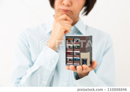 A middle-aged woman worries while holding a model of an apartment building. 110898846