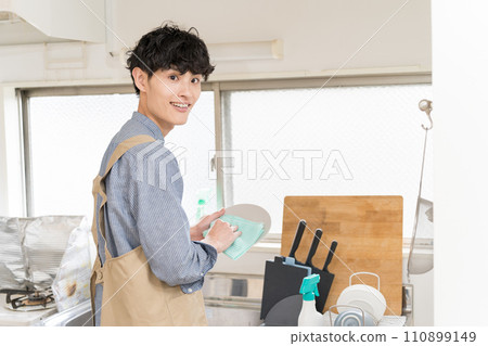 A young man who does housework by wiping dishes in the kitchen. Housekeeper 110899149
