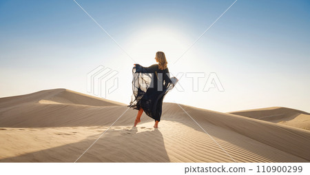 Desert adventure. Young arabian Woman posing in traditional Emirati dress abaya in sanddunes of UAE desert at sunset. The Dubai Desert Conservation Reserve, United Arab Emirates. Desert adventure. Young arabian Woman posing in traditional Emirati dress abaya in sanddunes of UAE desert at sunset. The Dubai Desert Conservation Reserve, United Arab Emirates. 110900299