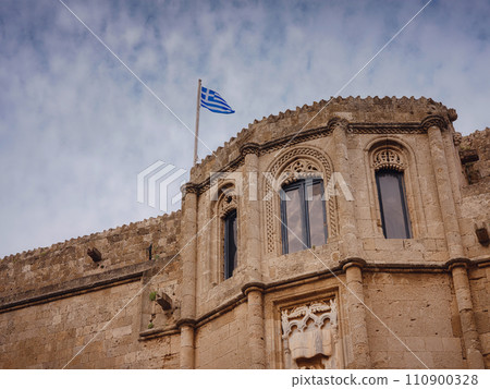 facade of an old beautiful building with the national Greek flag in sunset time. Travel to Greece, Mediterranean islands Rhodes. 110900328