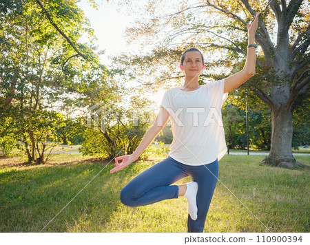 Young asian woman doing yoga in morning or evening at park, healthy woman relaxing and practicing tree pose at city park. Mindfulness, destress, Healthy habits and balance concept Young asian woman doing yoga in morning or evening at park, healthy woman relaxing and practicing tree pose at city park. Mindfulness, destress, Healthy habits and balance concept 110900394