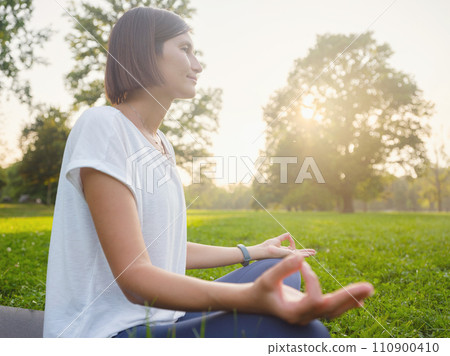 Young asian woman doing meditation in morning or evening at park, healthy woman relaxing and practicing yoga at city park. Mindfulness, destress, Healthy habits and balance concept 110900410