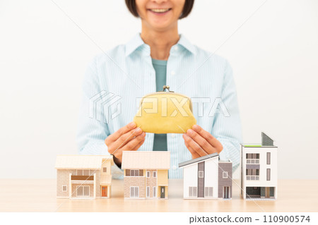 A smiling middle-aged woman holding a wallet and multiple house models A smiling middle-aged woman holding a wallet and multiple house models 110900574