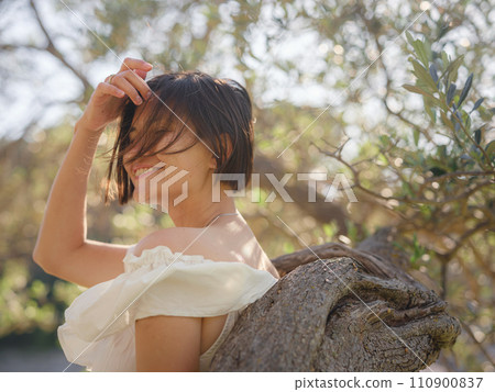 Beautiful Asian young woman in white dress outdoor near olive tree. embracing fresh air and engaging in outdoor activities. Friluftsliv concept means spending as much time outdoors as possible Beautiful Asian young woman in white dress outdoor near olive tree. embracing fresh air and engaging in outdoor activities. Friluftsliv concept means spending as much time outdoors as possible 110900837