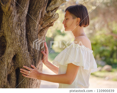 Beautiful Asian young woman in white dress outdoor near olive tree. embracing fresh air and engaging in outdoor activities. Friluftsliv concept means spending as much time outdoors as possible Beautiful Asian young woman in white dress outdoor near olive tree. embracing fresh air and engaging in outdoor activities. Friluftsliv concept means spending as much time outdoors as possible 110900839